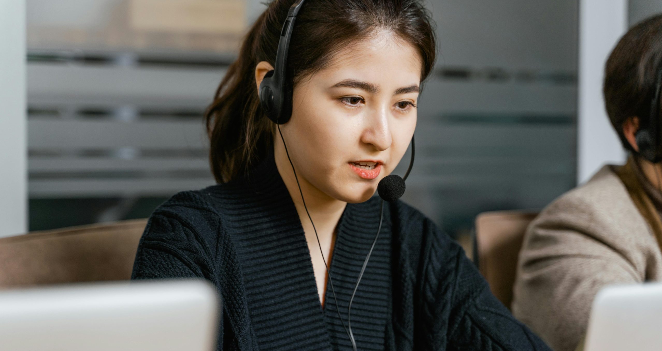 Asian woman in a call center focused on customer support tasks using a laptop.